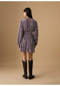 Dolga vijolična pletena obleka z dolgimi rokavi, z nazobčanim pasom in razširjenim krilom, kombinirana s črnimi škornji do kolen. Zadnji del ima izrez v obliki ključavnice.