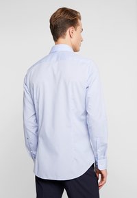 Camicia azzurro chiaro a maniche lunghe con texture liscia, polsini con bottoni e orlo curvo. Sono visibili strisce verticali.