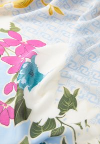 Foulard di seta con un motivo floreale che presenta fiori rosa, bianchi e turchesi su uno sfondo blu chiaro, accentuato da un sottile design geometrico.