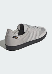 Zapatillas grises hechas de gamuza y malla, con un diseño de tres rayas, suela de goma negra y una etiqueta de Cordura en el talón.