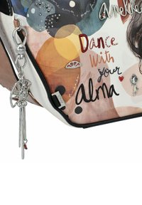 Mehrfarbige Handtasche mit grafischem Design, ausgestattet mit silberfarbenen Beschlägen, dekorativen Anhängern und dem Text "Tanze mit deiner Seele" auf einer strukturierten Oberfläche.