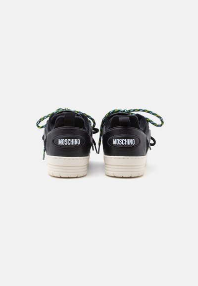 Ζευγάρι μαύρα αθλητικά παπούτσια Moschino με λευκές σόλες, εμφανιζόμενα από πίσω, με πράσινα και λευκά κορδόνια σε λευκό φόντο.