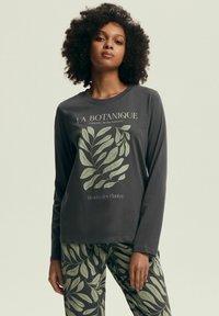 Szara koszula z długim rękawem w zielony botaniczny wzór i tekst. Koordynujące spodnie mają podobny wzór liści. Oba elementy wykonane są z miękkiego materiału.
