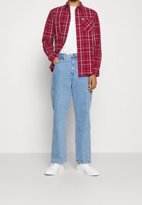 Červená a bílá kostkovaná košile s dlouhými rukávy, pod ní bílá tričko, doplněné světle modrými džíny s rovnými nohavicemi a bílými teniskami.