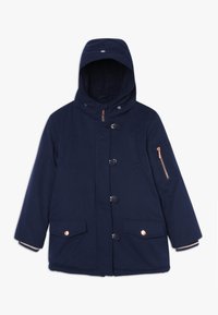 Abrigo de invierno con capucha en azul marino, con botones frontales, cremallera, dos bolsillos con solapa y broches, y un bolsillo con cremallera en la manga izquierda.