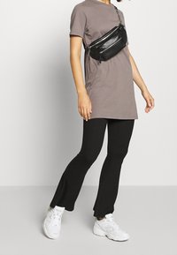 Persona che indossa un vestito t-shirt malva, pantaloni svasati neri con spacchi alle caviglie, sneakers bianche e una borsa a tracolla nera con zip argentate.