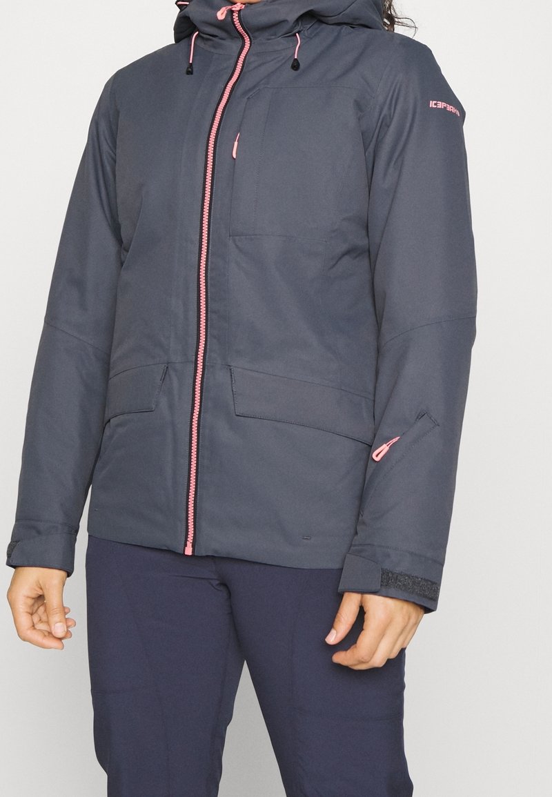 Granatowa kurtka ocieplana z różowym zamkiem błyskawicznym i sznurkami. Posiada podwójne przednie kieszenie oraz kieszeń na rękawie zapinaną na zamek. Gładka faktura.