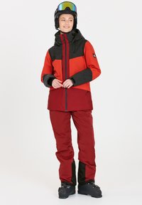 Ski-jack en broek set in rood en zwart. De jas heeft een kleurblokontwerp, een ritssluiting aan de voorkant en een verstelbare capuchon. Waterdicht materiaal.