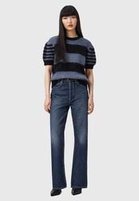 Gestrickter Pullover im gestreiften Blau- und Schwarzdesign, kombiniert mit einer dunklen Jeans. Robustes Material, lockere Passform und weit geschnittene Beine mit minimalen Details.