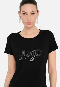 Zwarte t-shirt met een ronde hals en korte mouwen, met een glanzende zilveren grafische print van de merknamen op de borst.