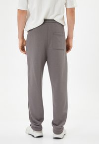 Pantalones de chándal grises con un corte relajado, cintura elástica y detalle de bolsillo trasero, fabricados en un tejido suave. Combinados con zapatillas blancas.