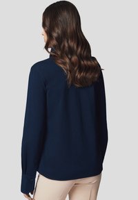 Granatowa koszula z długim rękawem i kołnierzykiem, wykonana z gładkiego materiału, z guzikami przy mankietach i luźnym krojem, widoczna z tyłu.