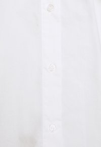 Camicia di cotone bianca con una texture liscia, chiusura frontale con bottoni trasparenti e un design del colletto classico.