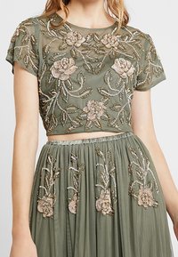 Borduurde crop top en rok set in olijfgroen. Bevat bloemmotieven in parels en pailletten, doorzichtige stof en een gegatherde taille.