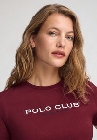 Camiseta corta de manga en color marrón con "POLO CLUB" bordado en blanco y azul, cuello redondo, tela suave y diseño entallado.