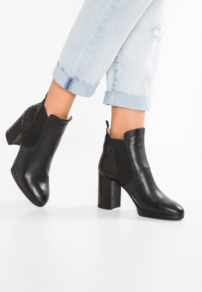 Bottines noires à la cheville avec une finition brillante, des accents noirs texturés et un talon carré haut. Matières : cuir et éléments synthétiques.