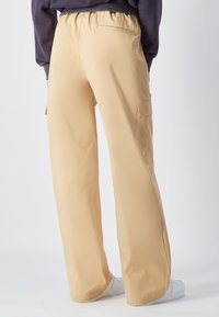 Beige cargobroeken met een elastische tailleband, rechte pijpen en zijzakken. Gemaakt van een soepele stof; gecombineerd met witte sneakers.