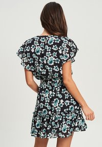 Vestido negro con flores turquesas y blancas, mangas con volantes, cintura ajustada y dobladillo con volantes en capas. Tejido ligero.
