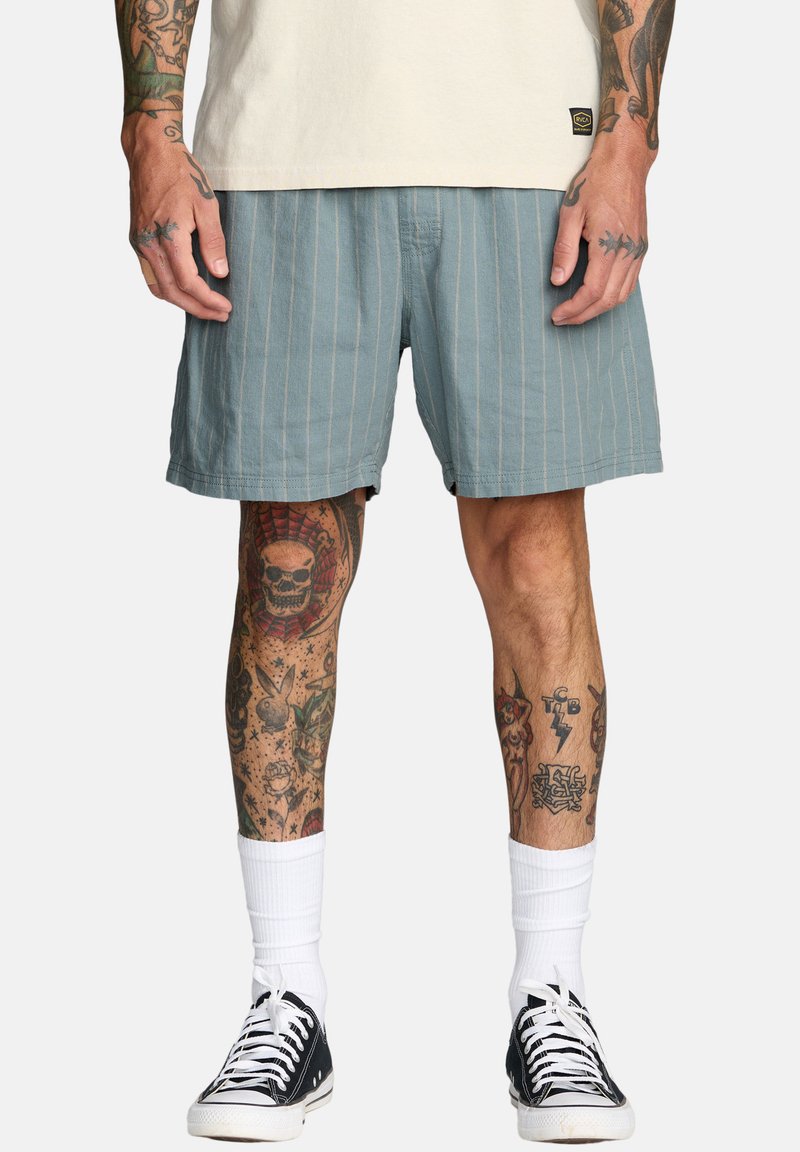 Męskie jasnoniebieskie szorty w paski z miękkiego materiału o luźnym kroju. Zestawione z czarnymi trampkami i białymi skarpetkami do kostek.