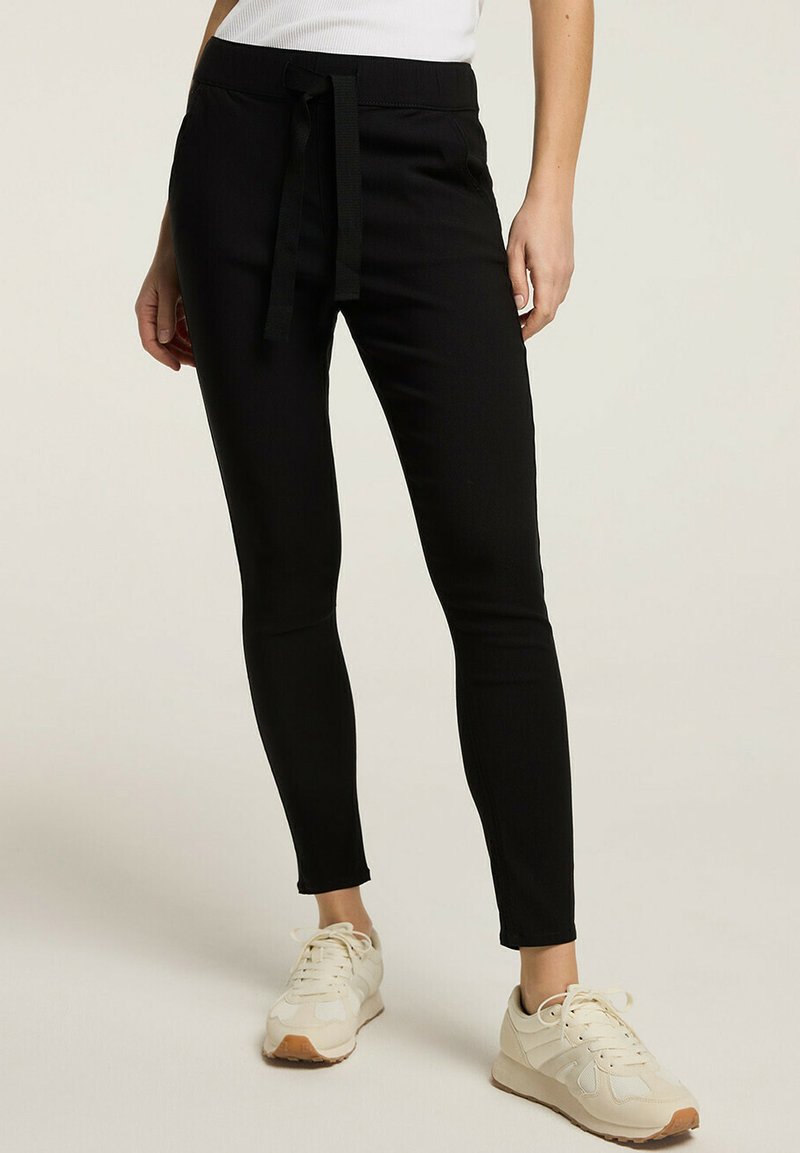 Czarne elastyczne spodnie o dopasowanym kroju, z elastycznym pasem i sznurkiem do regulacji z materiału. Posiadają gładką teksturę i zwężane nogawki.