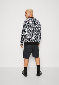 Svart-hvitt genser med abstrakt tigerstripemønster, ribbede mansjetter og kant, sammen med mørke cargo shortser og svarte sko.