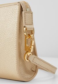 Beżowa torba ze strukturalnej skóry z zapięciem i zamkiem w kolorze złotym oraz cienkim paskiem przymocowanym z boku.