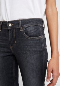 Dark denim jeans with a fitted cut, featuring subtle stitching, front pockets, and a metal button closure at the waistband.