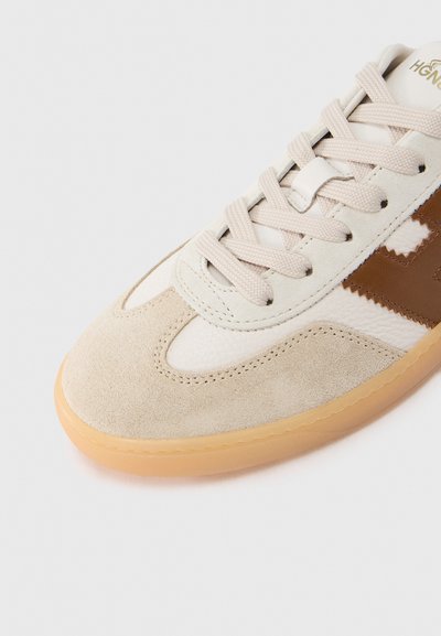 Μπεζ αθλητικό παπούτσι με συνδυασμό σουέτ και δέρματος, με σόλα από καουτσούκ, επίπεδους κορδόνια και καφέ λεπτομέρεια στο πλάι.