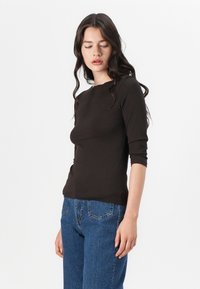 Svart langermet topp med rund hals, tettsittende design og myk stoff. Kombinert med blå høytlivsjeans med baklommer.