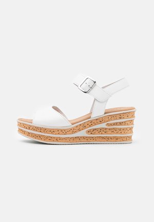 Białe sandały na koturnie z korkową podeszwą, z odkrytym palcem i regulowanym paskiem wokół kostki. Gładka skóra z teksturowanymi akcentami.