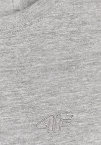 Gros plan d'un tissu gris avec le logo "4F" cousu près du bas à droite et un col côtelé en haut.