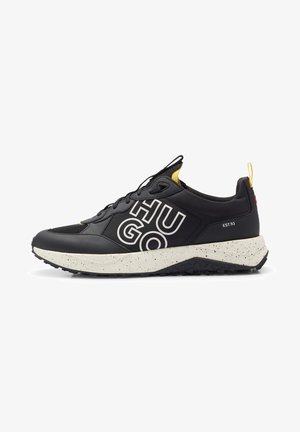 Zapatilla negra y amarilla con suela blanca salpicada, logotipo audaz "HUGO" en el lateral y texto "EST. 93" en el talón.