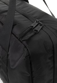 Sac de sport noir en tissu nylon texturé, avec des fermetures éclair doubles et des poignées de transport robustes. Forme rectangulaire, design compact.