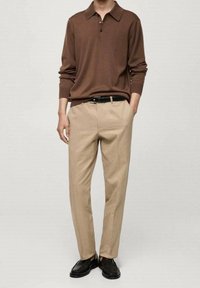 Braunes Langarm-Polohemd mit Kragen und drei Knöpfen, kombiniert mit hellbeigen Hosen und schwarzen Schuhen. Glatter Stoff.