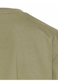 Lys olivegrøn bomulds t-shirt med rund hals, korte ærmer og en glat tekstur. Sømme er synlige rundt om kraven og skuldrene.