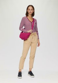 Gestreepte bordeauxrode en witte lange mouwen top met knopen, beige corduroy broeken en een roze schoudertas. Zwarte sneakers maken de outfit compleet.