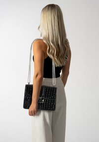 Borsa nera in pelle con stampa cocco, con una tracolla in argento, forma rettangolare elegante e dettaglio della serratura nella parte frontale. La finitura testurizzata aggiunge interesse visivo.