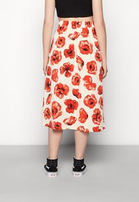 Kukkakuvioinen midi-hame, jossa on punaisia unikoita kermanvärisellä pohjalla, joustava vyötärönauha ja yhdistetty mustien korkeavartisten tennareiden kanssa.