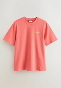 T-shirt rose corail à manches courtes avec col rond et petit texte jaune "AMALFI COAST" sur la poitrine gauche.