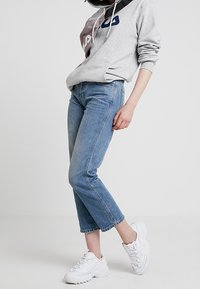 Sudadera gris con capucha y detalles en bloque de color, jeans azules de corte recto y zapatillas deportivas blancas.