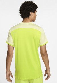 Camiseta deportiva para hombre en un brillante amarillo neón con mangas cortas. Presenta una sección inferior texturizada y un diseño liso en los hombros superiores.