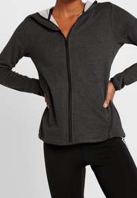 Felpa con zip di colore grigio scuro, con una fodera interna grigia, design aderente, maniche lunghe e tasche laterali. Tessuto morbido e testurizzato con dettagli cuciti.