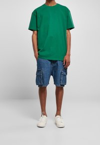 Zelené bavlněné tričko s krátkým rukávem doplněné modrými džínovými cargo šortkami s dvěma velkými bočními kapsami. Bílá tenisky dotvářejí celkový vzhled.