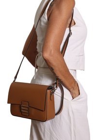 Borsa a tracolla in pelle marrone con una forma strutturata, chiusura a pattina e accessori metallici. Include una tracolla removibile.