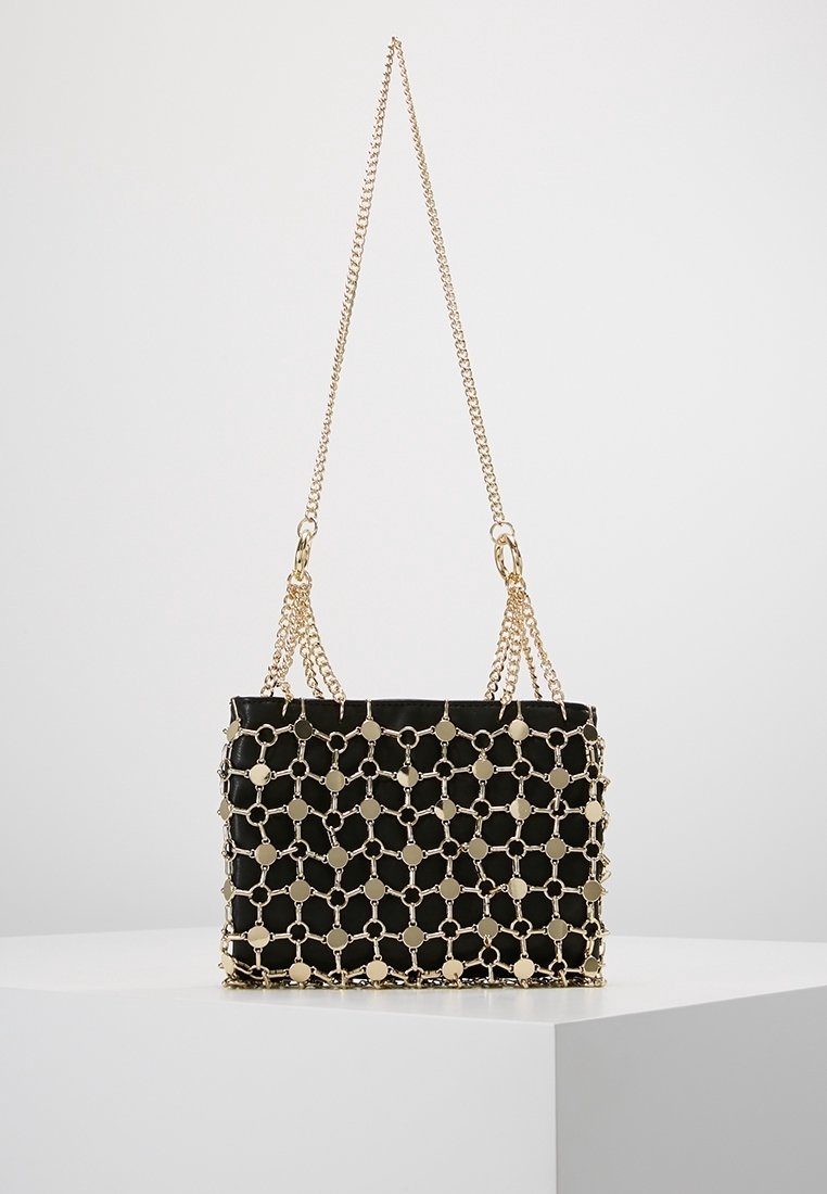 Bolso rectangular negro con revestimiento de red de cadena dorada y doble asa de cadena dorada, expuesto sobre una superficie blanca.