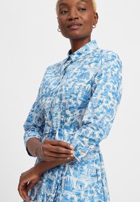 Weißes Hemdkleid mit blauem Landschaftsprint, ausgestattet mit einem Knopfkragen, langen Ärmeln und einem taillierten Bund. Glatter Baumwollstoff.