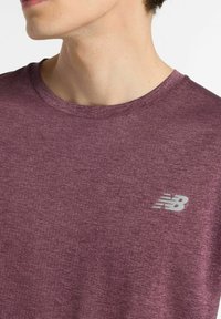 Maroon athletic t-shirt with a round neckline and textured fabric. Features a small gray New Balance logo on the chest.