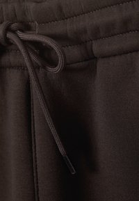 Bruine sweatpants met een trekkoordsluiting, een zachte stoffen textuur en zichtbare naden. Ze hebben een relaxed fit en een minimalistisch ontwerp.