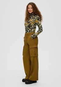 Langsleeve, slimfit top met een multikleurig bloemmotief. Bruine cargobroek met wijde pijpen en zijzakken. Zwarte plateau schoenen.