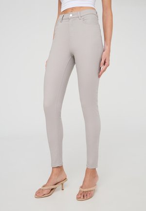 Jeans skinny a vita alta grigio chiaro con una texture liscia, dotati di tasche frontali, passanti per cintura e chiusura con zip.